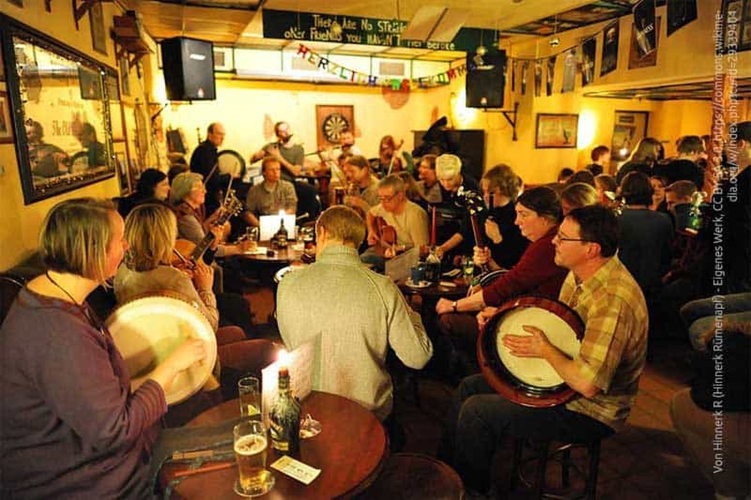 A lively folk music session in a packed British pub with yellow walls, featuring various traditional instruments and patrons enjoying beers.